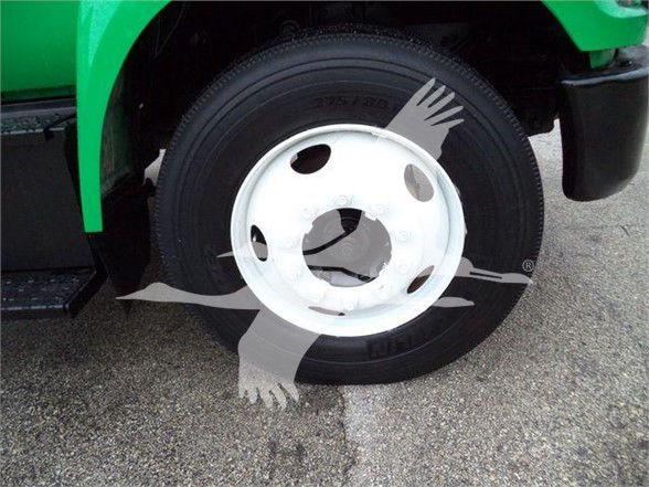 Ford F-Series dump truck wheel visible with tire and white steel rim. Partial fender and green bodywork are visible.