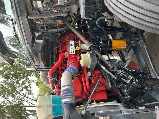 Truck engine bay of a 2020 Peterbilt 579 showing a red engine, blue radiator hose, various wiring, and fuel/wlter filters.