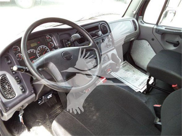 Truck interior showing steering wheel, dashboard, and driver seat of a Freightliner M2. Visible instrument cluster and center console with some papers on the floor mat.