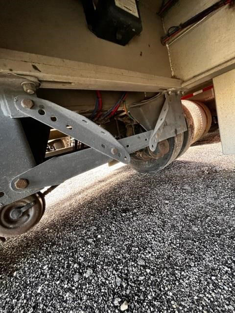 Trailer undercarriage showing wheel axle and mounting brackets with rollers and cables; rolling tarp system visible at rear.
