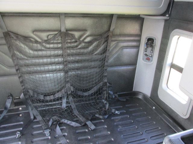 Truck sleeper cab interior with netted seat/storage, window, and control panel on right side. Text visible: none clearly legible.
