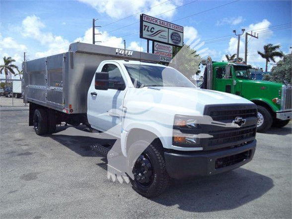 Chevrolet Silverado 6500HD dump truck in a dealership lot with aluminum dumping bed, white cab, and green truck in background.