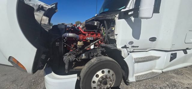 Kenworth T680 truck engine bay visible through open hood showing red engine components and front wheel.