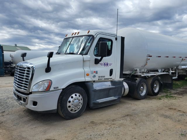 Freightliner Cascadia truck cab and tanker trailer in a gravel lot with overcast sky.