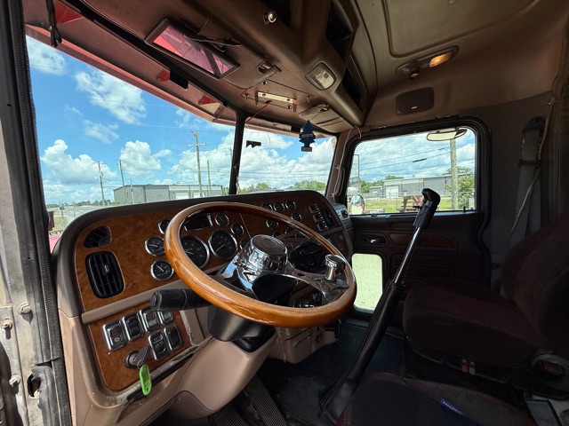 Truck cab interior showing steering wheel and dashboard with wood veneer panels and numerous gauges.
