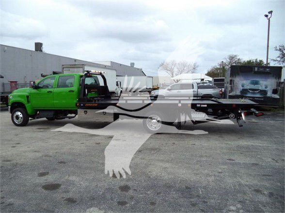 Green tow truck tractor unit with flatbed trailer, side view showing cab and hitch.