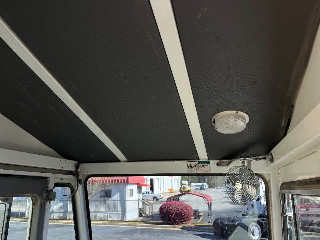 Interior cab roof with a round dome light, vent, and a small fan mounted on the right side; outside shows equipment and yard.