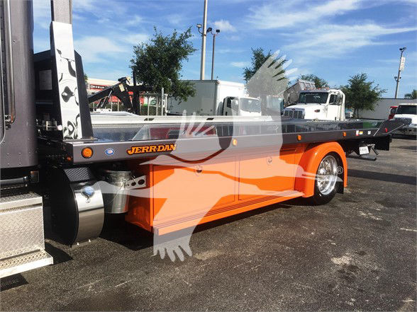 Peterbilt 337 tractor with orange frame on a trailer in a dealership lot, JERR-DAN branding on the side rail.