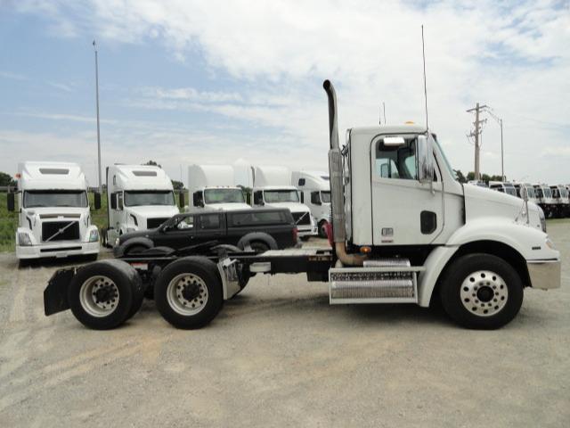Truck side view showing a white Freightliner Columbia tractor with dual rear axles and a bare chassis. Series of white trucks in background.
