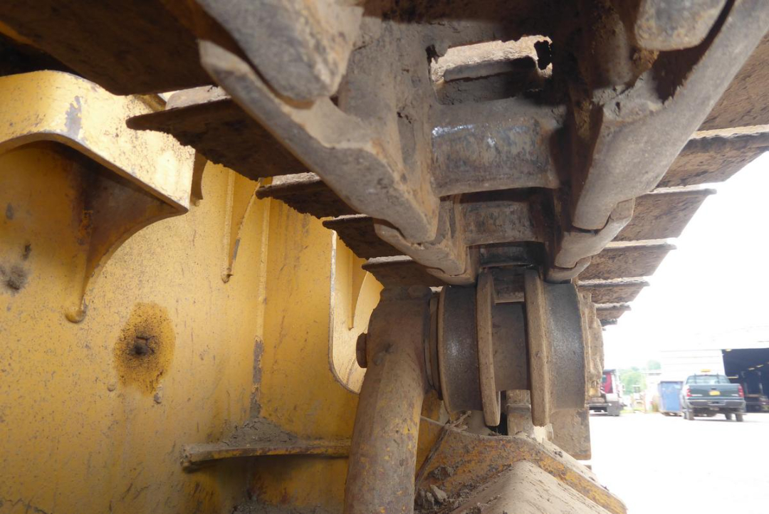 Tracked excavator undercarriage showing rubber track, rollers, and yellow painted frame.