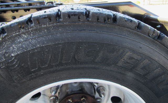 Truck wheel showing Michelin tire with tread and rim; partial fender and undercarriage visible.