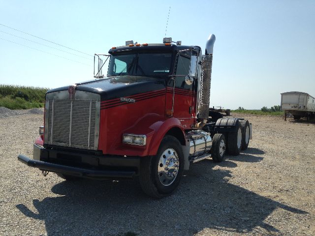 Kenworth T800 conventional daycab truck in red and black, chrome grille, large fuel tanks, dual rear axles, cab steps, exhaust stack on the passenger side.