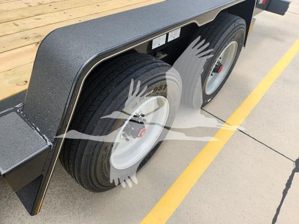 Flatbed trailer undercarriage showing dual rear axles with white wheels and black tires, fender with textured surface, concrete parking lot lines.
