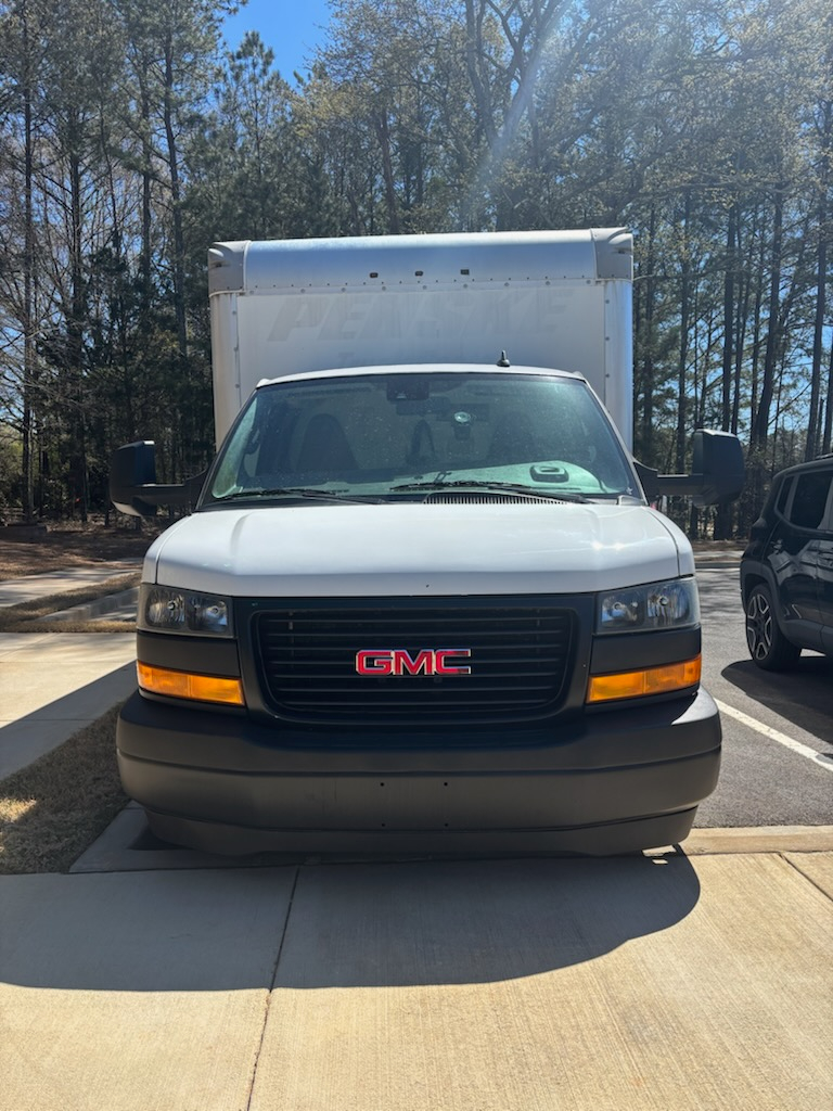 GMC Savana 3500 front view showing GMC grille and headlights with orange turn signals, box cargo truck behind in outdoor lot.