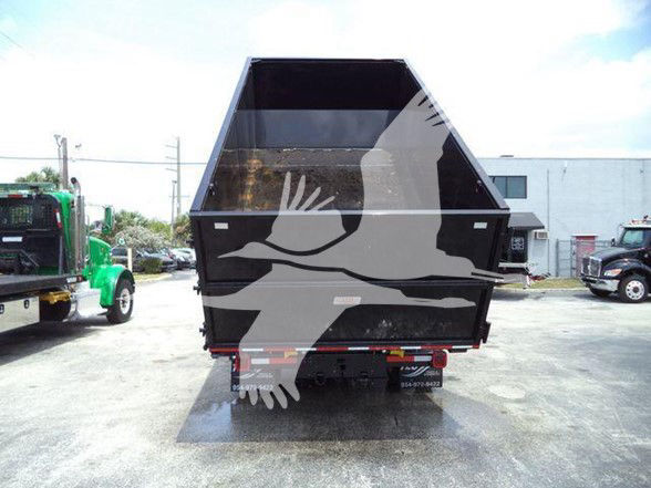 Truck rear view of a 2023 Chevrolet Silverado 6500HD dump bed with black hopper, in-service landscape lot.