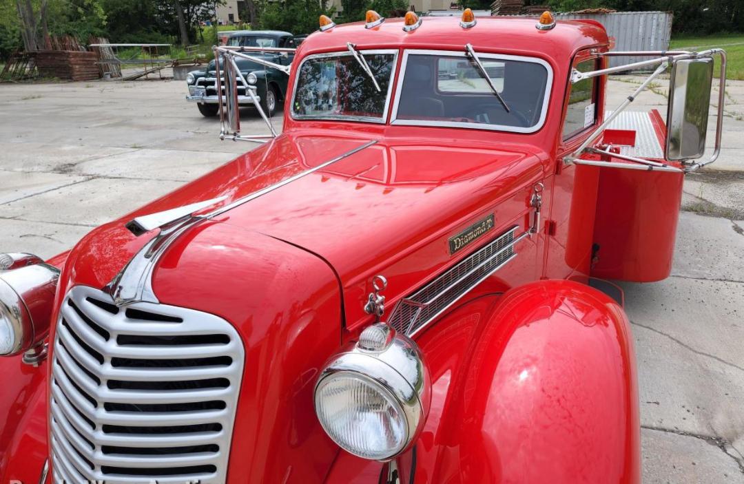 Diamond T hauler truck showing bright red vintage cab with chrome grille, round headlight, hood ornament, and diamond badge on the side.