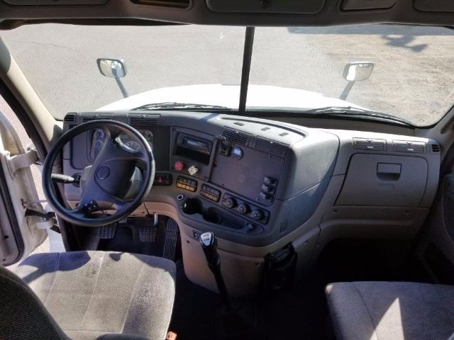 Truck cab interior of a 2012 Freightliner Cascadia showing steering wheel, dashboard with gauges, center console, gear shift, and driver seat.