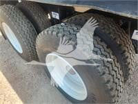 Trailer axle with dual tires showing heavy tread and wheel hub. Visible label tags and part of frame