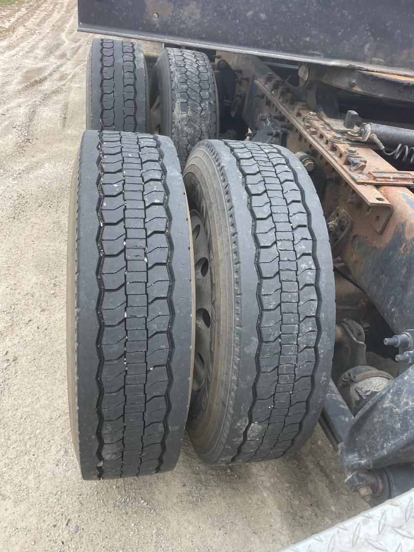 Truck rear dual wheels showing treaded tires and suspension components of a Freightliner Cascadia 125. Visible are four tires, steel wheel, and rusty chassis with leaf springs.