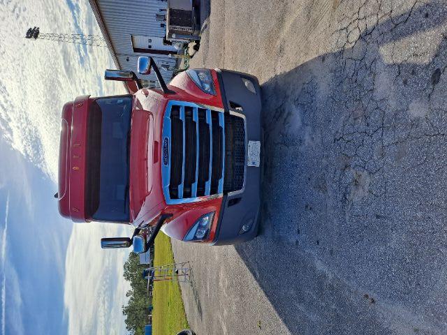 Front view of a red Freightliner Cascadia truck with chrome grille and large side mirrors.