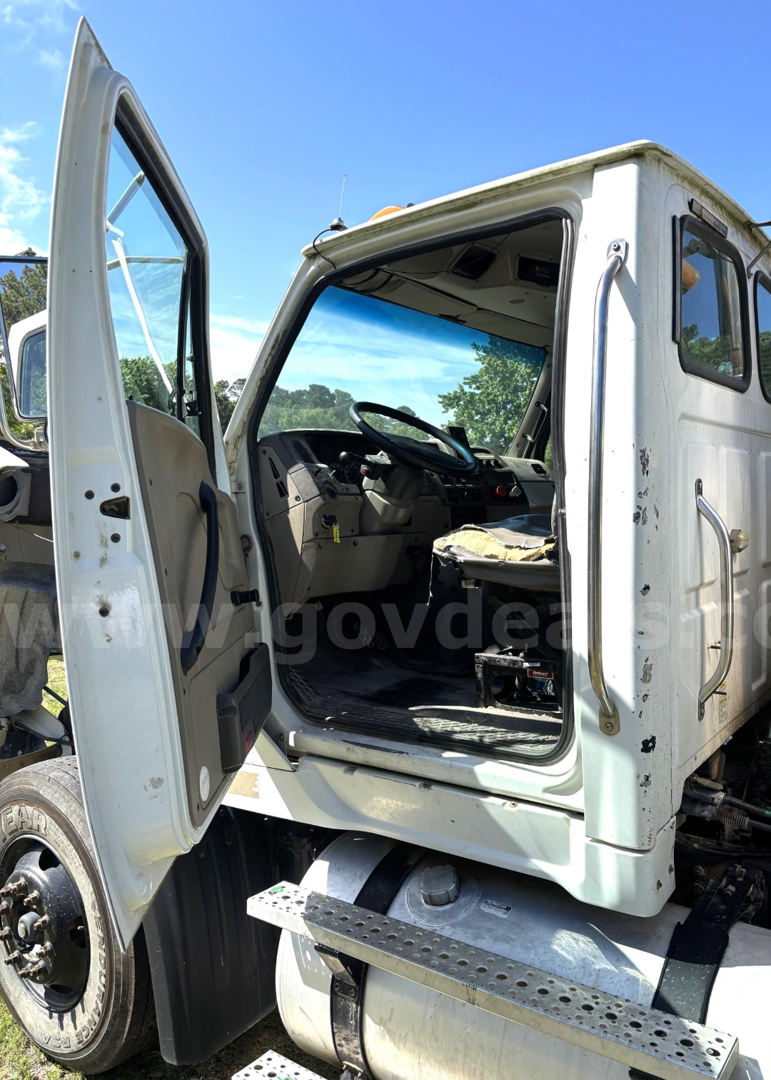 Cab and chassis truck cab interior visible through open door with steering wheel and dashboard; steps and wheel visible.