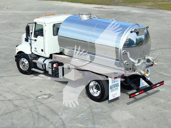 Tank truck with a shiny stainless steel cylindrical tank mounted on a white cab chassis, rear hoses and valves visible.