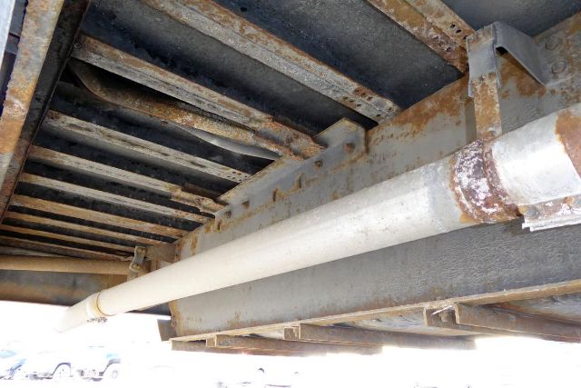 Underbody view showing rusted frame rails and a white cylindrical pipe running along the underside of a Freightliner FS65 bus.