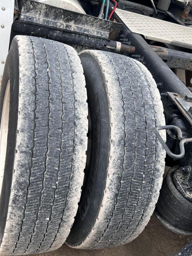 Freightliner Cascadia truck dual rear tires showing tread and mud, with suspension and frame components in view.
