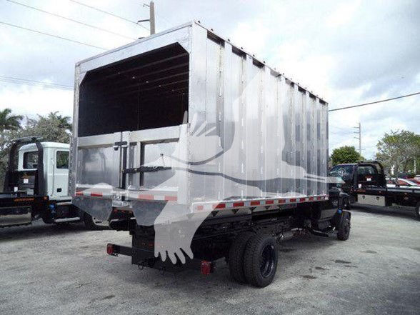 Tractor-trailer style truck with a large metal dumping bed and dual rear wheels, side view, in a dealership lot.