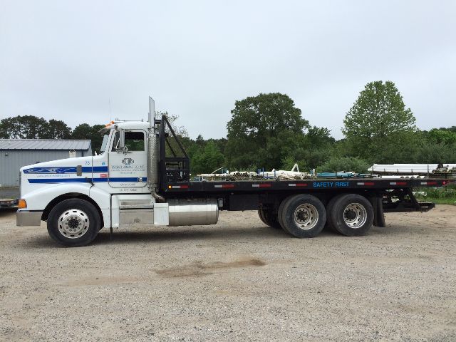 Peterbilt 377 rollback truck side view with long flatbed, showing text on cab and frame. Visible labels include company name and contact details on the door, and safety markings on the flatbed. 