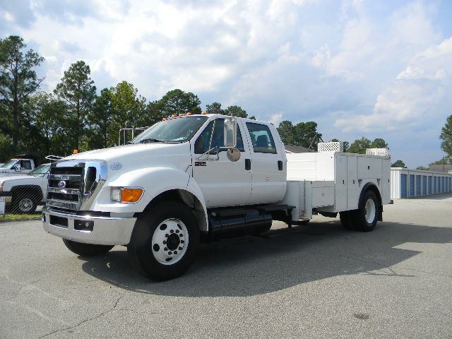 Ford F-750 Super Duty crew cab utility truck in white, side view, with service body compartments and dual rear wheels.
