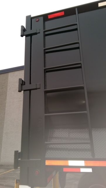 Dump trailer rear end with ladder and hinge latches, dark gray paint, reflective safety stripes on lower edge.