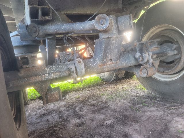 Walking floor trailer undercarriage showing suspension beam and axle with wear/soil on metal components.