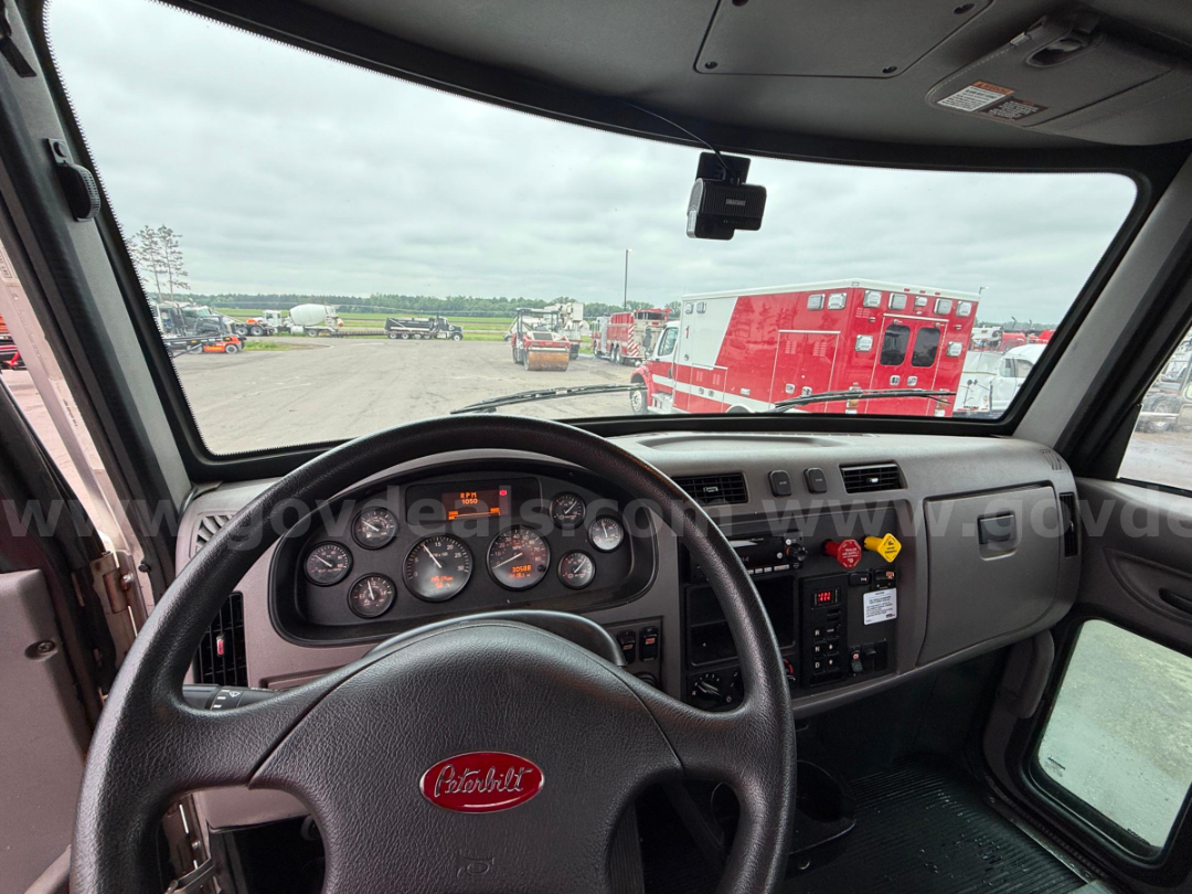 Peterbilt truck cab interior with steering wheel and dashboard, view through windshield showing red emergency vehicles outside.
