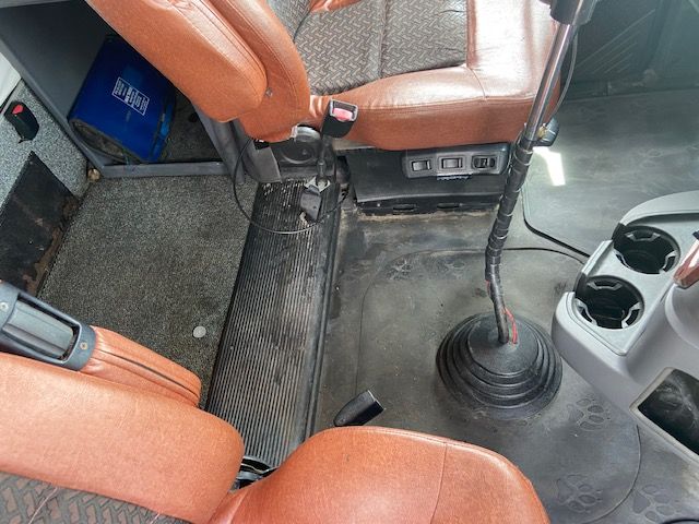 Cockpit view of a 2010 Mack CXU613 conventional sleeper showing the gear shifter, tan/orange seats, and floor area with console and cup holders.