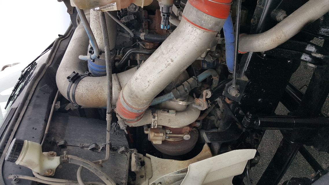 Engine bay of a 2007 International 8600 with visible turbocharger and large exhaust/air intake piping, hoses, and coolant reservoir.