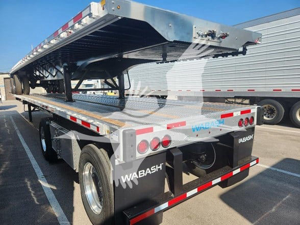 Wabash flatbed trailer in parked lot showing rear and ramp deck with multiple taillights, reflective tape, and WABASH branding.