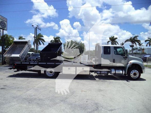 Tow truck with a white cab and flatbed, two dump beds or containers on the bed, side view showing cargo area and wheel wells.