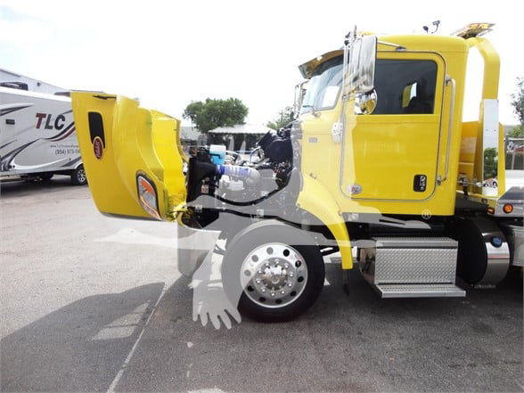 Yellow 2022 Peterbilt 337 tow truck with cab open revealing interior; side steps, large front wheel, and rear chassis visible.