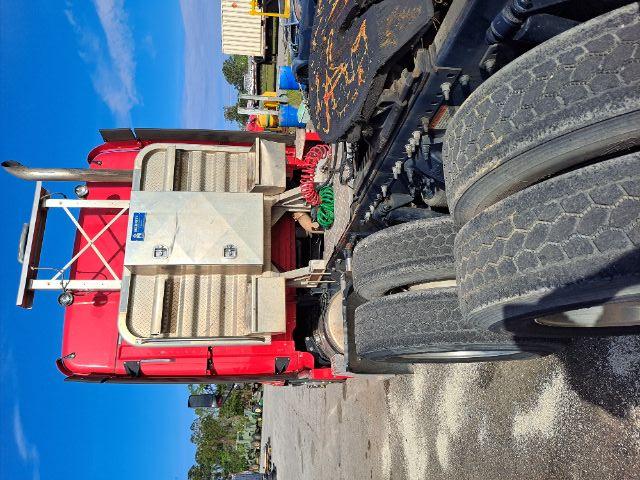 Rear view of a red Freightliner Cascadia tractor cab with dual rear axles and large aluminum battery/air intake housing; visible chrome exhaust stack and hoses.