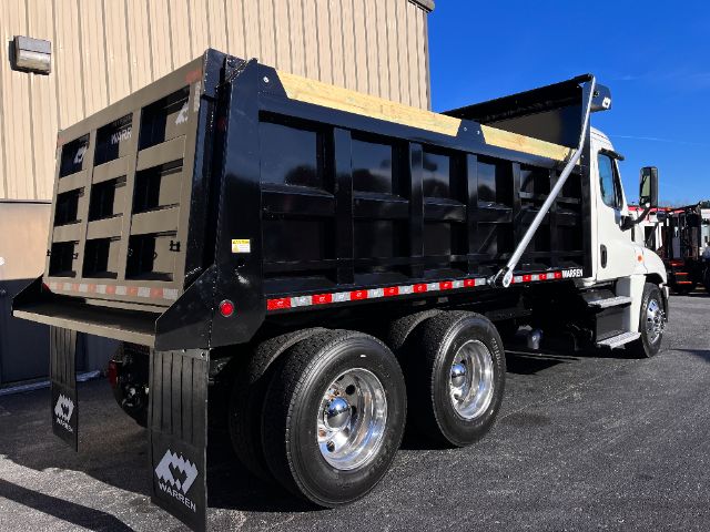 Dump truck bed and cab of a Freightliner Cascadia 125 dump truck, black dump body, dual rear axles, white cab with Warren mud flaps.