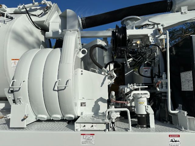 Industrial vacuum truck side showing large hose reel, pump components, and control panel in a white service body.