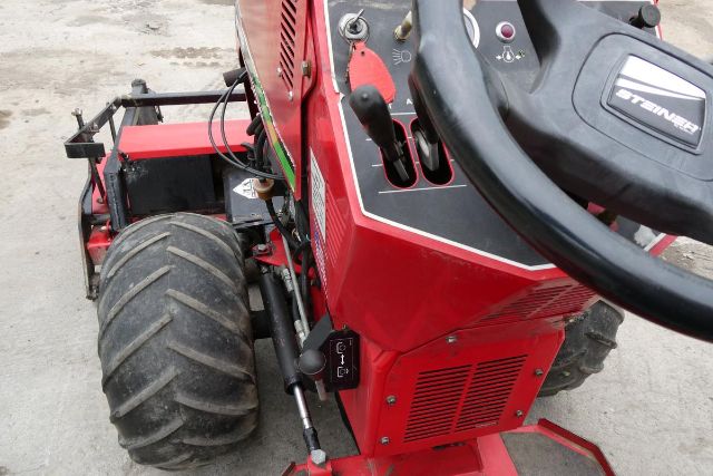 Steiner 415 agricultural equipment with red cab and steering wheel, close-up of controls and large rear tire.
