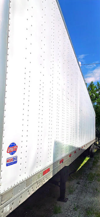 A white utility trailer with riveted aluminum side panels, lower reflective tape, and a blue sky background.