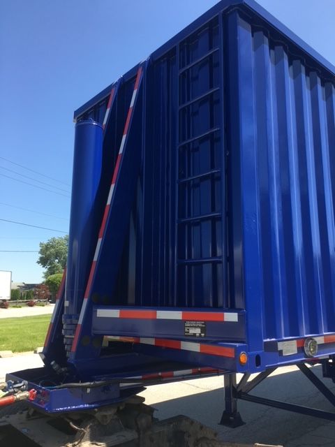 Blue 40 ft utility dump trailer with ribbed side panels and reflective white/orange stripes; rear door and hydraulic system visible.