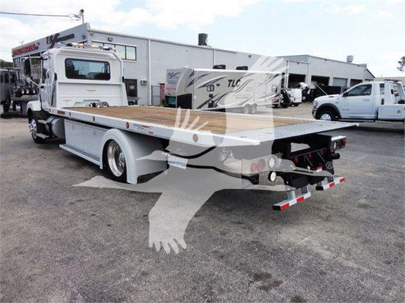 Side view of a white 2025 Mack MD6 tow truck with a flatbed and extended rear; stock number J04370; new unit on a dealership lot.