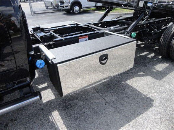 Ram 5500 chassis cab with a rectangular aluminum toolbox mounted on the side frame near the cab. Tow truck chassis visible in background with black paint.