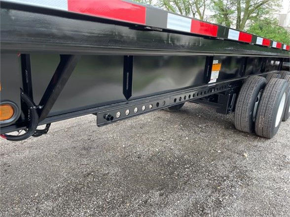 Flatbed trailer side view showing I-beam frame and underbody crossmembers with extendable section, black paint, and tandem axles.