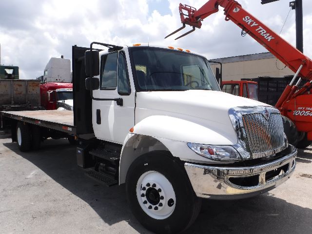 2018 International 4300 flatbed truck with extended cab, white cab, black chassis, and flatbed; large chrome grille and dual rear wheels visible.