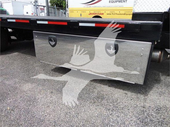 Flatbed truck storage box mounted under Silverado 6500HD rear with polished stainless steel toolbox showing two circular keyholes and a reflection of birds in flight.